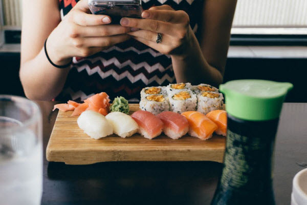 Woman using a mobile phone with sushi on her table